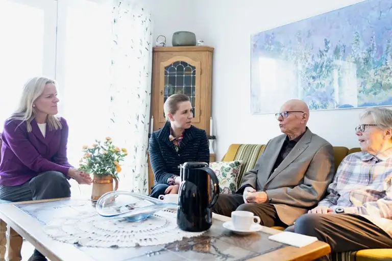 Mette Kierkgaard og Mette Frederiksen i sofasnak med to ældre personer